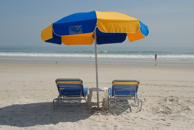 2 transats jaune et bleu face à la mer, avec un parasol au dessus, de la même couleur que les transat.